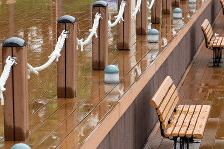 Lonely new marina after the rain, with wet wooden decks and benches, and a fence strung with ropes.