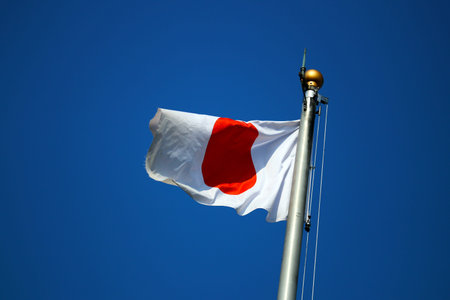 National flag of Japan flaps in the wind. Bright blue sky background.