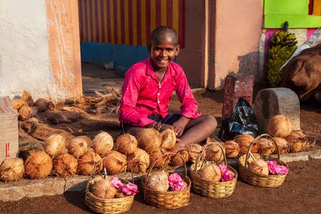 HAMPI, INDIA - FEBRUARY 21, 2012: Unidentified boy selling coconut offerings for holi puja in Delhi, Indiaのeditorial素材