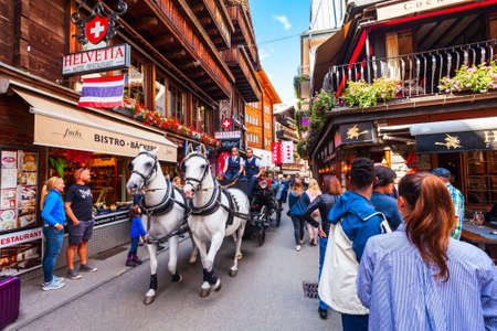 ZERMATT, SWITZERLAND - JULY 15, 2019: Horse coach and traditional local houses in the centre of Zermatt town in the Valais canton of Switzerlandのeditorial素材