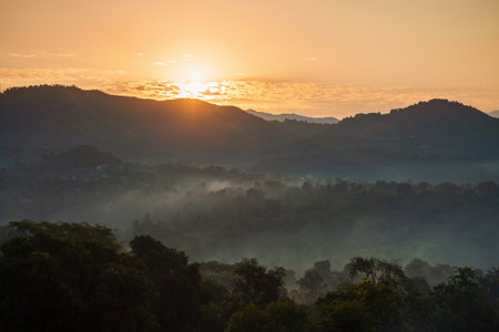 Scenic landscape view of the forested mountain slope in mist and clouds at sunrise, Himalaya mountains in Himachal Pradesh, Indiaの写真素材