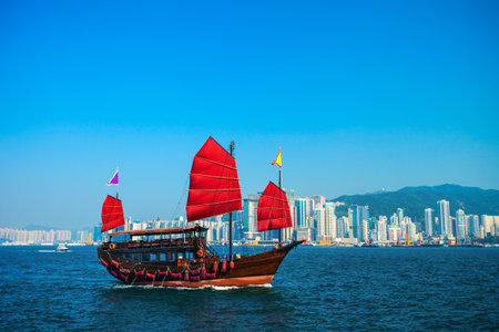 Tourist traditional style cruise sailboat with red sails crosses Victoria harbor from Kowloon to the Hong Kong 
Islandの写真素材