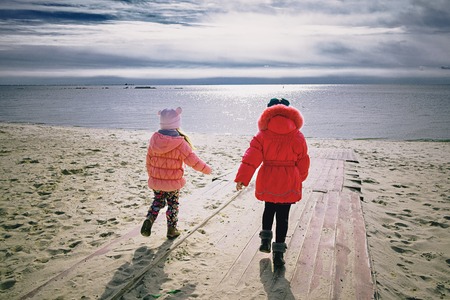 Two little girlfriends running to the sea after winterの写真素材