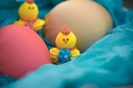 Three toy chickens and three easter eggs on the grass in a blue basketの写真素材