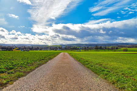 A landscape with clouds and a road to a village in a fieldの写真素材