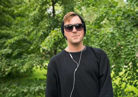 Man in black clothes is listening to music on the street.