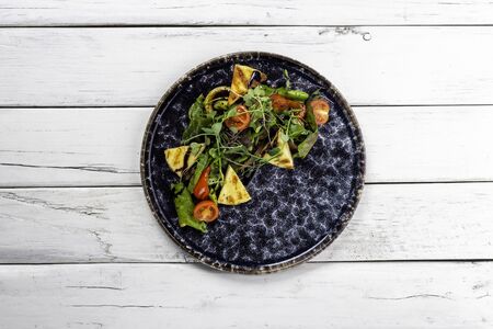 salad with grilled cheese, tomatoes and green on a white wooden backgroundの写真素材