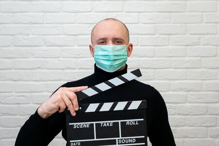 Man in black pullover in virus mask with clapperboard on white backgroundの写真素材