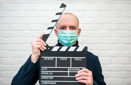 Man in dark blue jacket in virus mask on white with clapperboardの写真素材