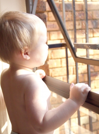 Little boy is looking through the window with barsの写真素材