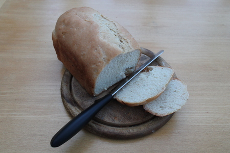 Sliced fresh home baked loaf with knife on wooden cutting board, wooded table の写真素材