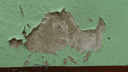 Peeling paint on green wall reveals textured surface underneath, creating interesting visual.
