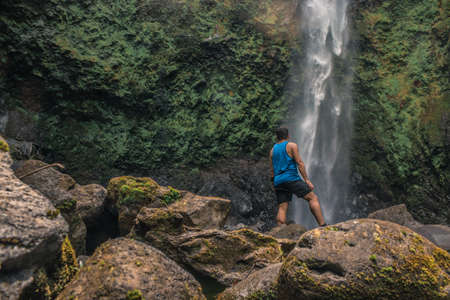 Costa Rica, SarapiquÃ­ de Alajuela, Cariblnaco, El Congo Waterfall. Young man at the base of a waterfall admiring the green and deep landscapeの写真素材