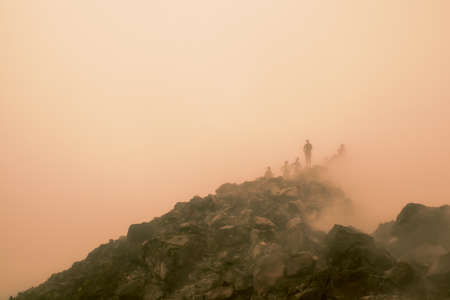Peak of Arenal Volcano, Alajuela, Costa RIca. Landscape of the volcanic and desolate peak with some silhouettes of people in the background amid the fog and underground steamの写真素材