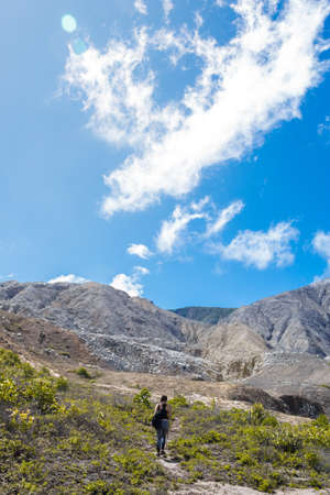 Quemaderos del PoÃ¡s, PoÃ¡s Volcano National Park, Alajuela, Costa Rica. young female hiker walks through a steep rock mountain and sparse vegetation on a sunny day with blue skyの写真素材