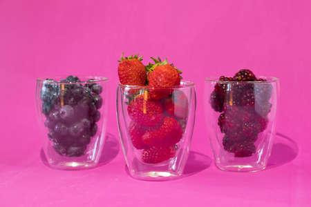 A few clear glass glasses with strawberries with blueberries and blackberries on a pink backgroundの写真素材