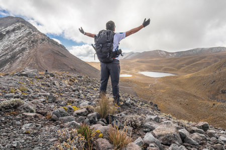 man with arms outstretched towards the landscape with rocky mountains and a lake on a sunny day