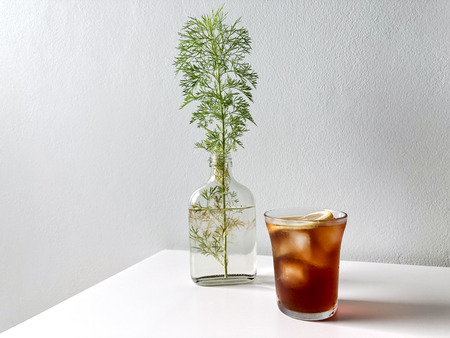 Iced pouring light roasted coffee, topped with lemon. On the white table with coriander plants in flat bottle.の写真素材
