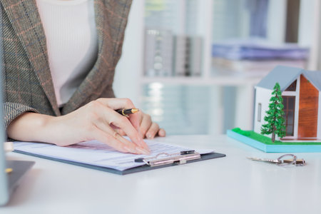 Close-up of woman's hand signing contract with house model and keysの写真素材