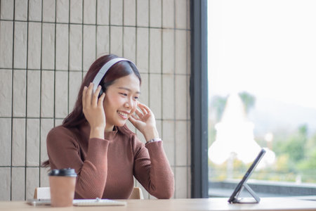 Young Asian woman wearing headphones using laptop in coffee shopの写真素材