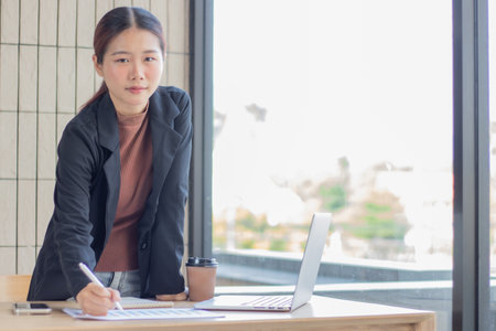 Portrait of a beautiful smiling business woman working at a modern work station and using a laptop to keep track of company income and expenses.の写真素材