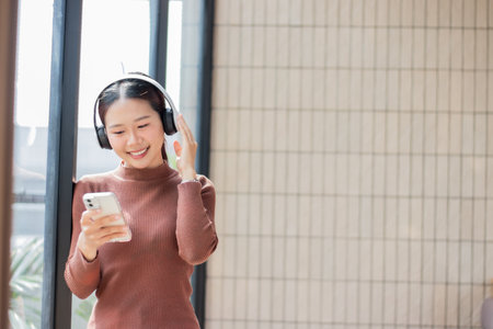 Beautiful young woman standing by the mirror with headphones on and smiling happily