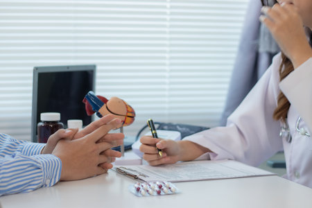 A young man with heart disease visits a female doctor for advice on heart disease treatment. The cardiologist shows a model of the anatomy of the human heart.の写真素材