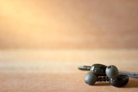 Closeup black In-ear monitor earphones on brown wood background in morning light.の写真素材