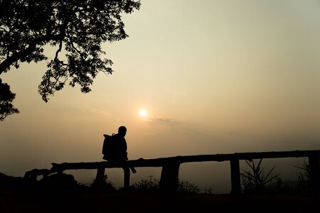 Silhouette lonely men sitting at the view point watching the sunset go down in among the mountains on evening.の写真素材