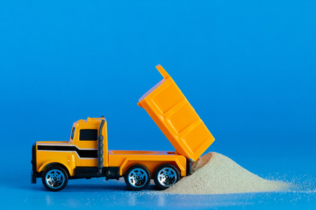 Yellow toy tractor is digging and lift sand on the blue background. Concept of construction.の写真素材