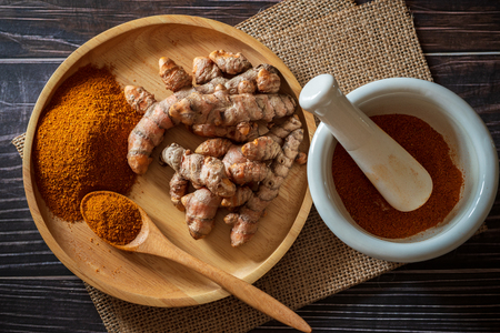 Turmeric powder and turmeric root on wooden dish with mortar and pestle on hemp mat in morning sunlight. Concepts of herbal medicine and health care.の写真素材
