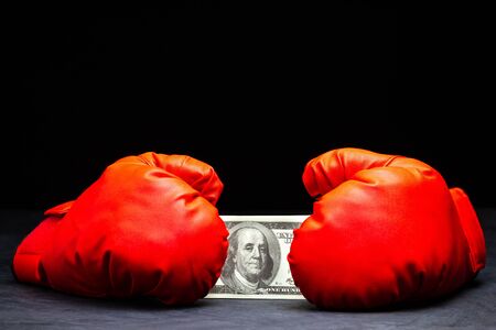 Red boxing gloves holding the dollar banknote on cement floor in darkness. Concept of fighting for money or business battles.の写真素材