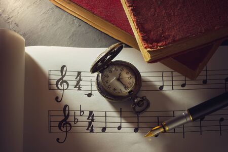 Music notes and old book with pocket watch on wooden table background in morning light. Writing chords by vintage pen. Closeup and copy space for text. Concept of Music lovers.の写真素材