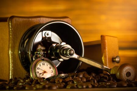 Coffee bean and pocket watch. Manual grinder on table in morning.