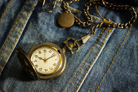 Vintage pocket watch is placed over an old blue denim shirt and the morning sun shines down in the top right corner. The concept of time importance. Closeup and copy space for text or your article.の写真素材