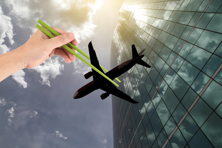 Hand hold a chopsticks tong a plane on a building background - Art concept.の写真素材