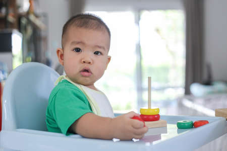 A baby of asia wearing bright green clothes is playing rainbow tower toys.の写真素材
