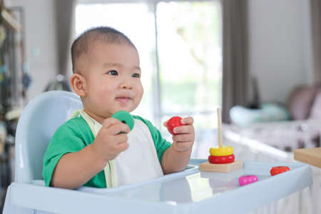 A baby of asia wearing bright green clothes is playing rainbow tower toys.の写真素材