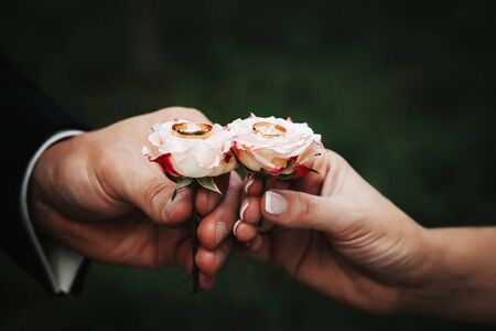 Couple holding two wedding rings placed on the roses. Close up image.の写真素材