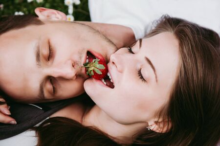 Young loving couple outdoors lying on grass eating strawberry.の写真素材