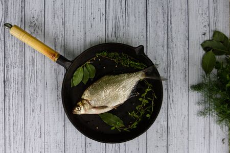 Fresh river fish bream on black cast frying pan, dill, laurel leaf, thyme, oregano, coriander.の写真素材