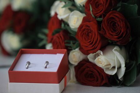 A close up marriage rings in box with red and white roses
