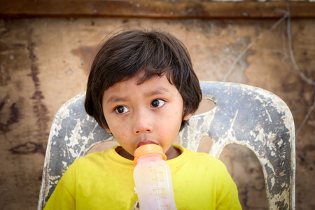 poor, sad little child boy sitting in the chair dirty concrete wall background .の写真素材