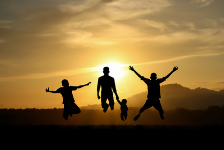 silhouette of father and boys jumping with joy at sunsetの写真素材