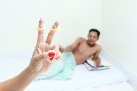 Woman hand holding three piece condom, while the man is lying on the bed.Safe sex concept.の写真素材