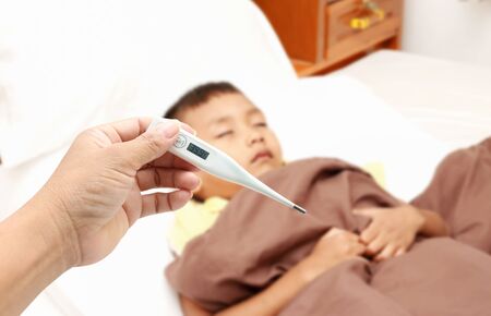 Mother hand holding fever thermometer for a boy ,who has fever on bed.