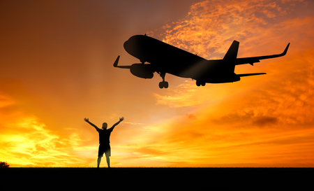 Silhouette of man posing for photo on the beach at sunset with an airplane landing.の写真素材