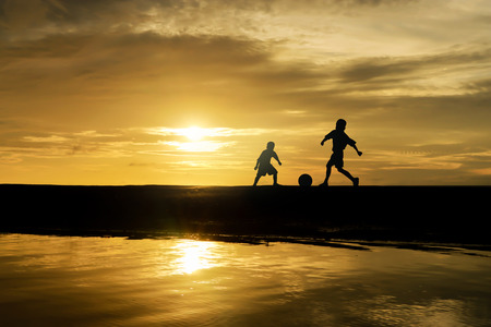 Two brothers boys play football at sunset.の写真素材