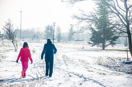 A girl and man walking in snow in Amsterdam. The girl is in her red jacket and pink pants. The man wears a blue jacketの写真素材