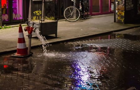 Water leaking thriugh the pipes in rotterdam netherlands in the night. Bike in the foot path in the backgroundの写真素材